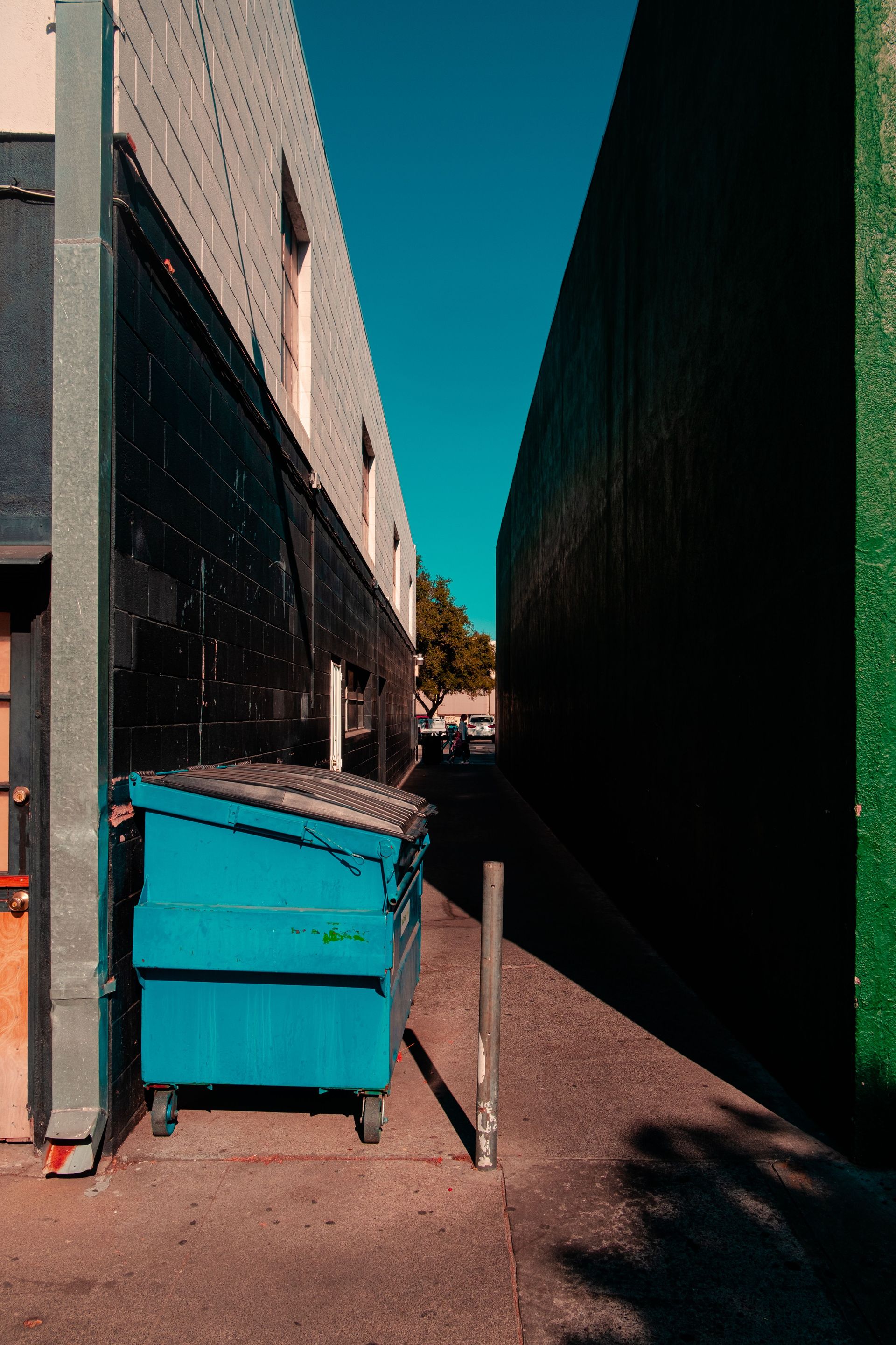 Narrow alleyway with contrasting sunlit walls and a blue dumpster, urban setting.